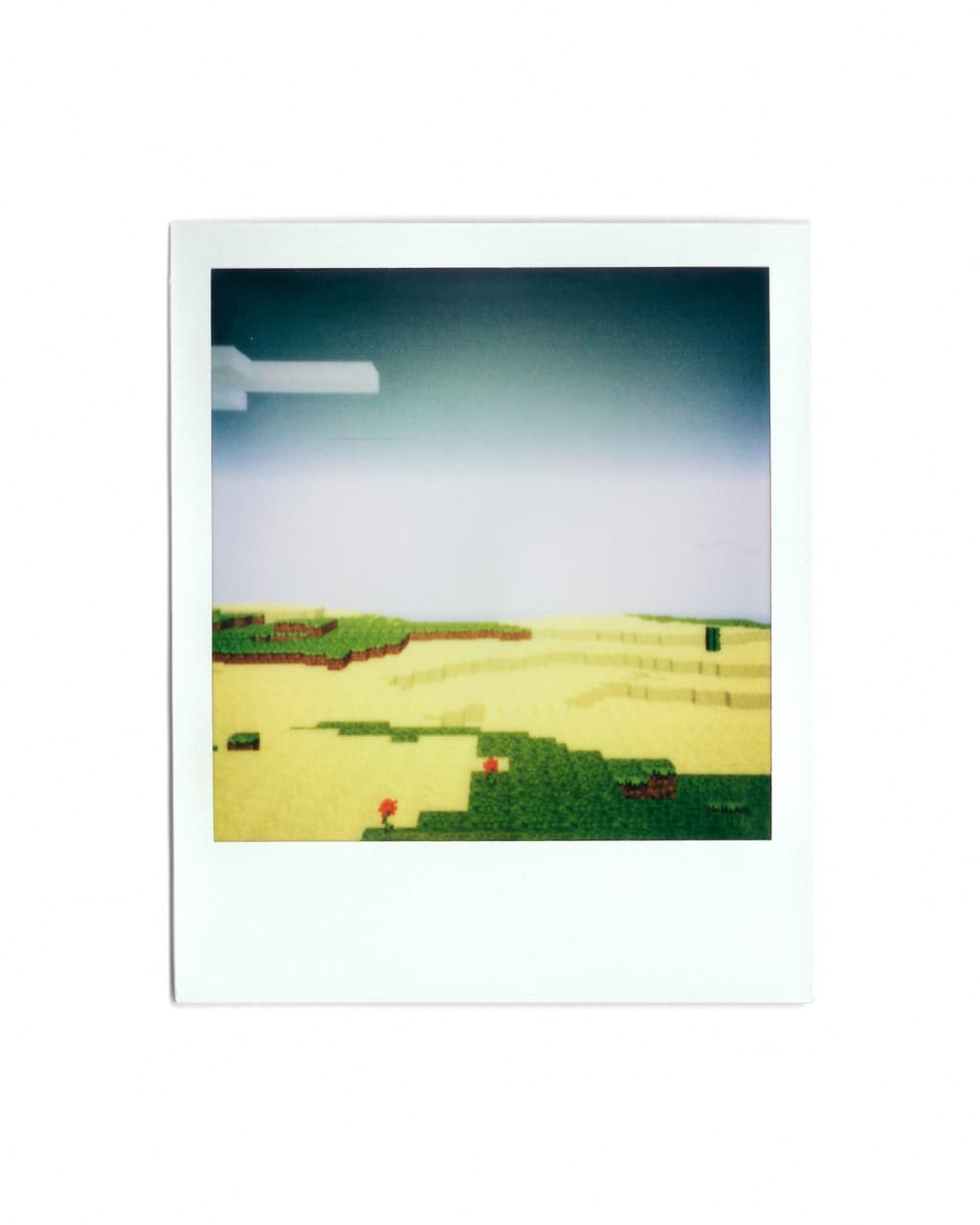 Polaroid print of a pale green shoreline and sand blocks under a bright sky.